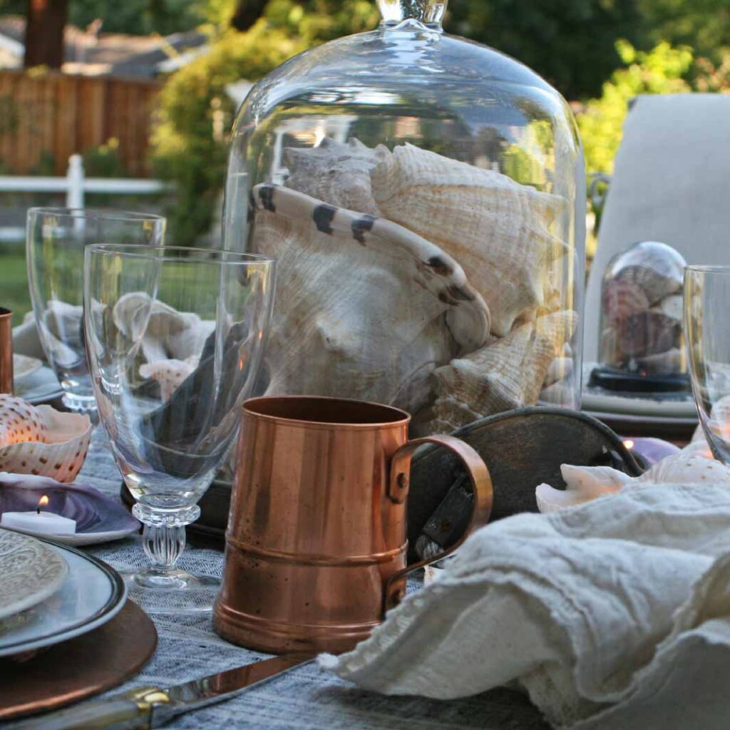 Seashells in cloches and copper tablescape outside on back patio
